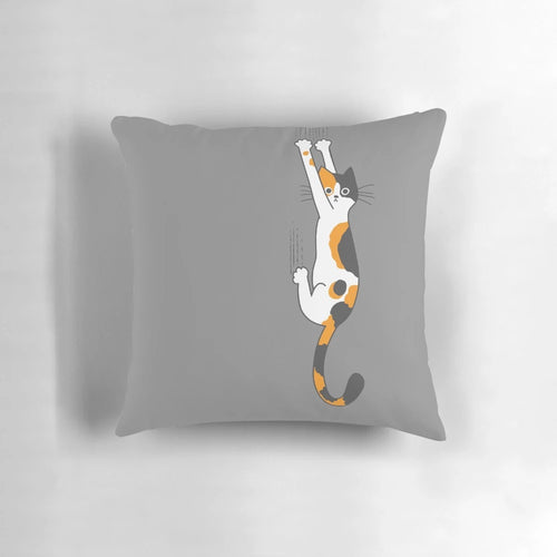 Calico cat humorously clinging to a plush throw pillow