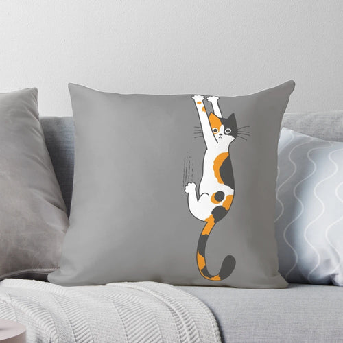 Calico cat humorously clinging to a plush throw pillow