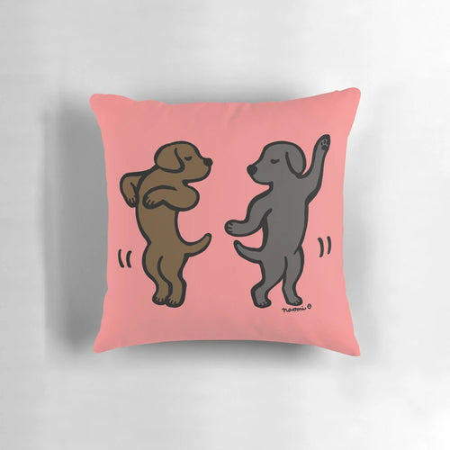 Playful cartoon illustration of a black labrador and a chocolate labrador dancing together on a decorative pillow