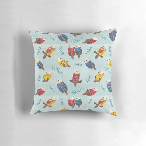 Illustration of two cute, chubby sea otters wearing a plaid, flannel pattern on a decorative pillow.