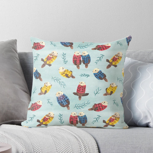 Illustration of two cute, chubby sea otters wearing a plaid, flannel pattern on a decorative pillow.