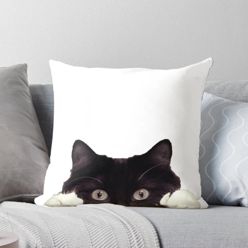 Cute black and white tuxedo cat peeking out from a cozy pillow