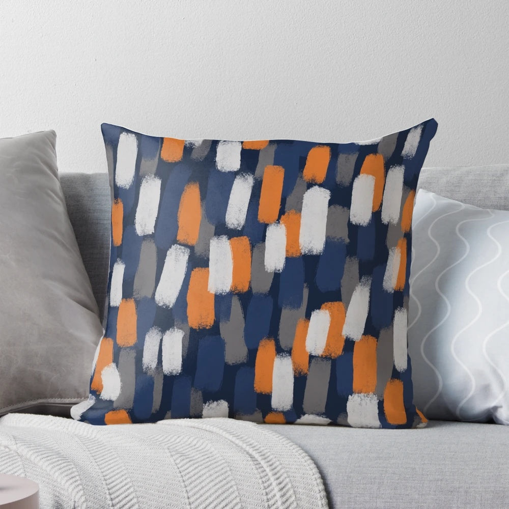 A decorative throw pillow featuring an abstract paint brush design in shades of gray, orange, and blue.