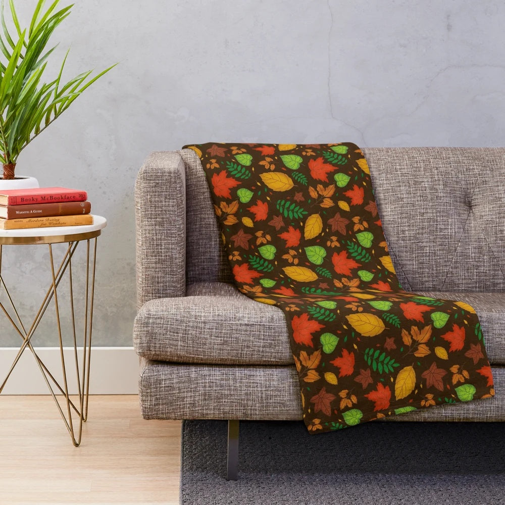 Plush blanket featuring a vibrant autumn leaves pattern in shades of orange, green, and yellow on a brown background