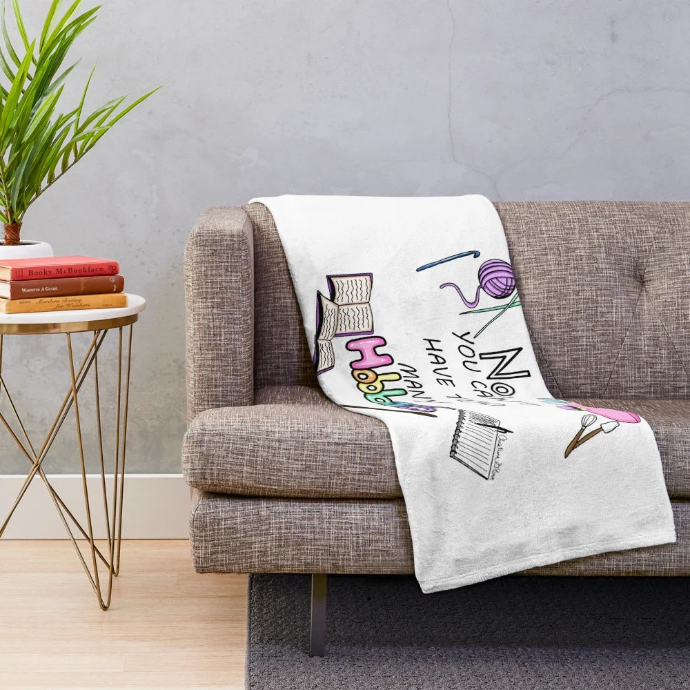 Plush blanket with a pastel rainbow design and illustrations of hobbies and crafts