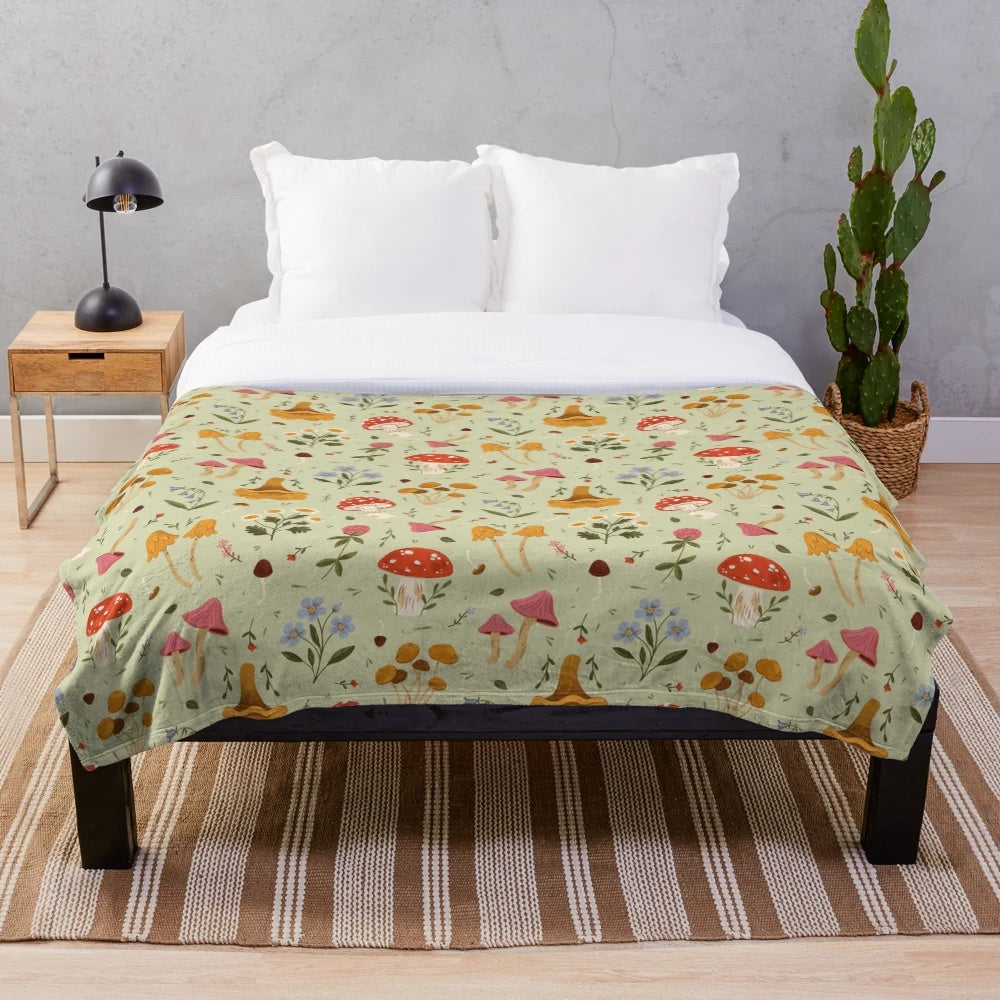 Plush blanket featuring artistic illustration of mushrooms and wildflowers in a natural, woodland setting