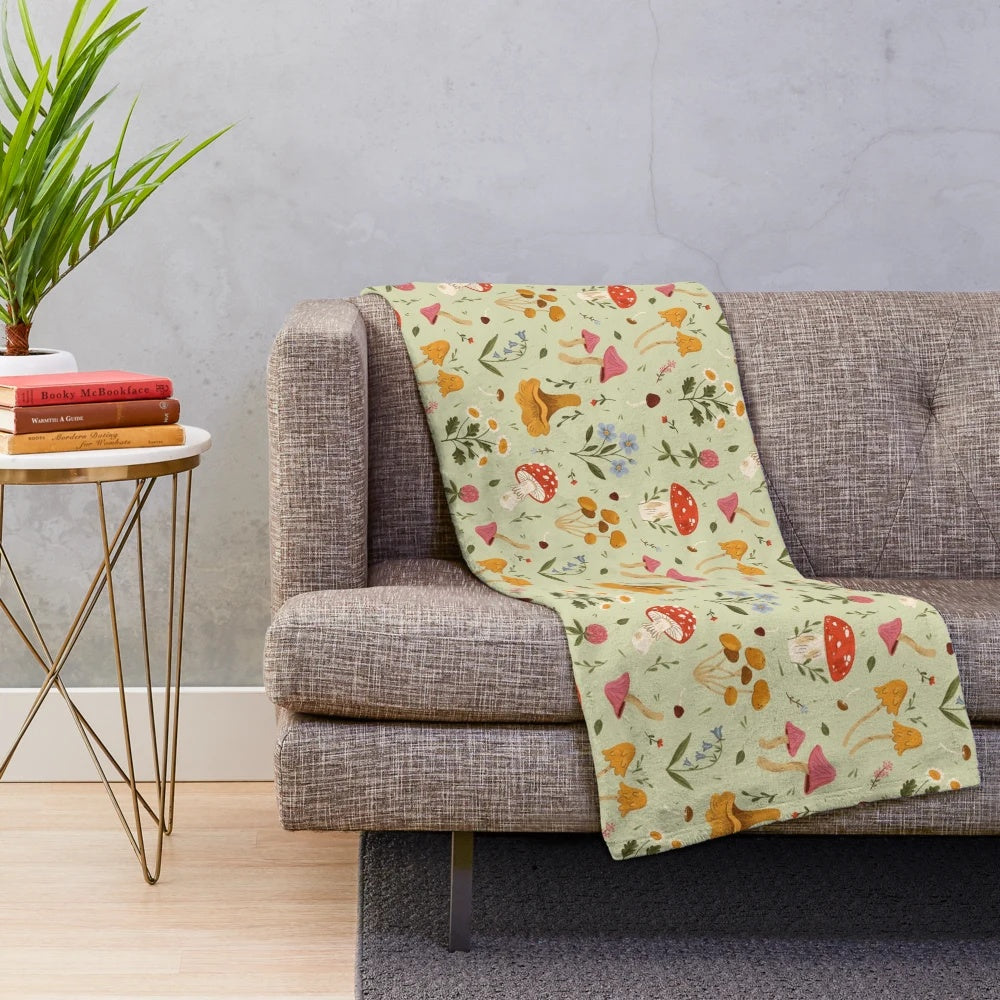 Plush blanket featuring artistic illustration of mushrooms and wildflowers in a natural, woodland setting