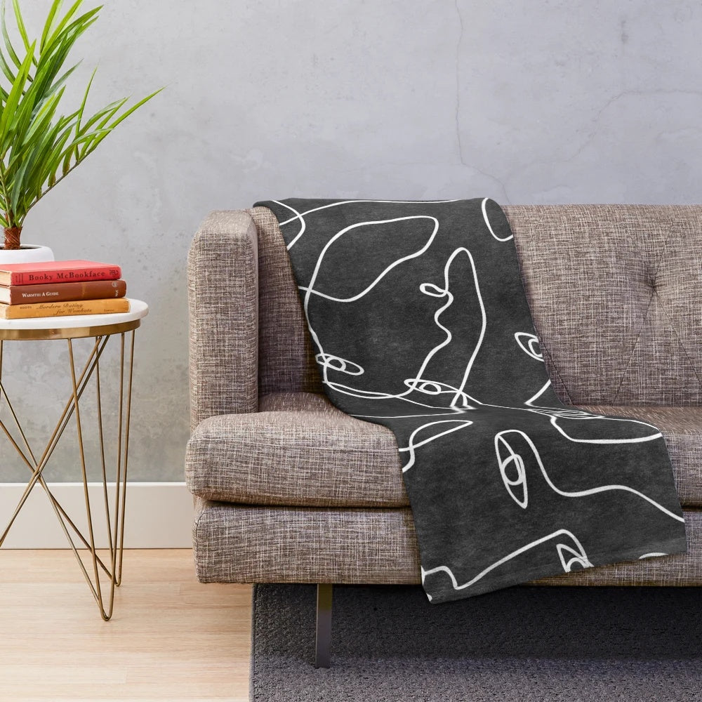 A soft and cozy plush blanket featuring abstract line art faces in a modern, minimalistic black and white design.