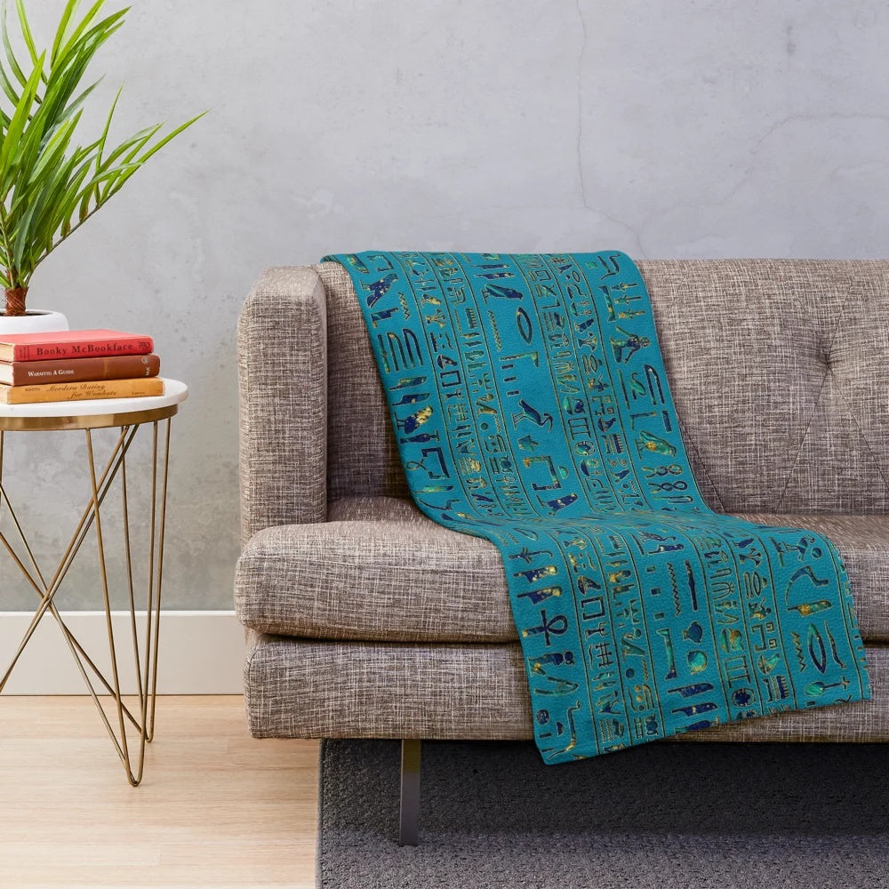Plush blanket with intricate egyptian hieroglyphic design on teal leather-like texture