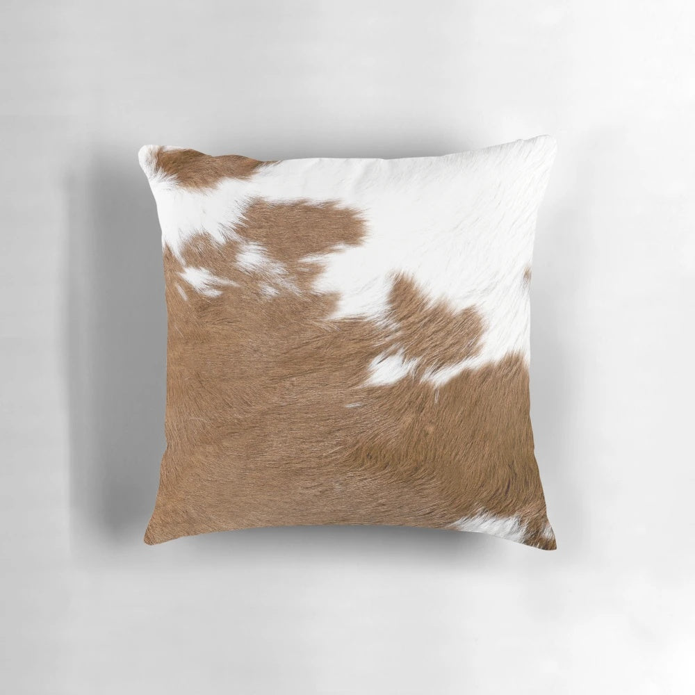 Rustic cow hide-inspired decorative pillow in brown and white tones, perfect for farmhouse or western-style home decor.