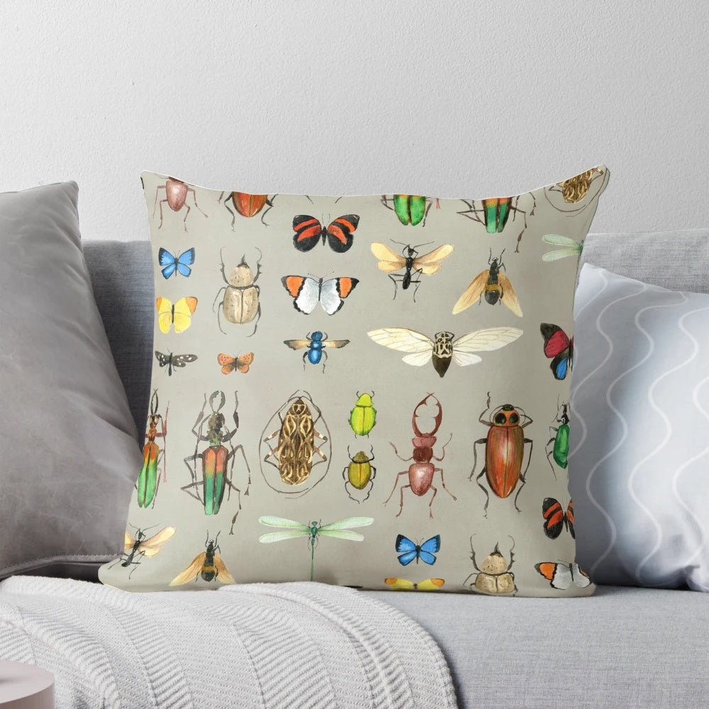 Watercolor illustration of various insects including butterflies, dragonflies, and beetles on a gray background, featured on a decorative pillow.